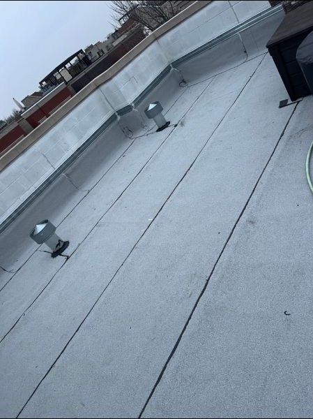 Completed light-colored flat roof with metal vents and parapet walls